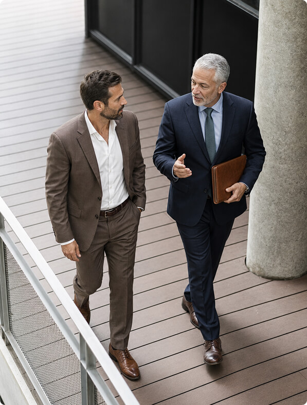 Two businessmen in suits walking and talking on a balcony